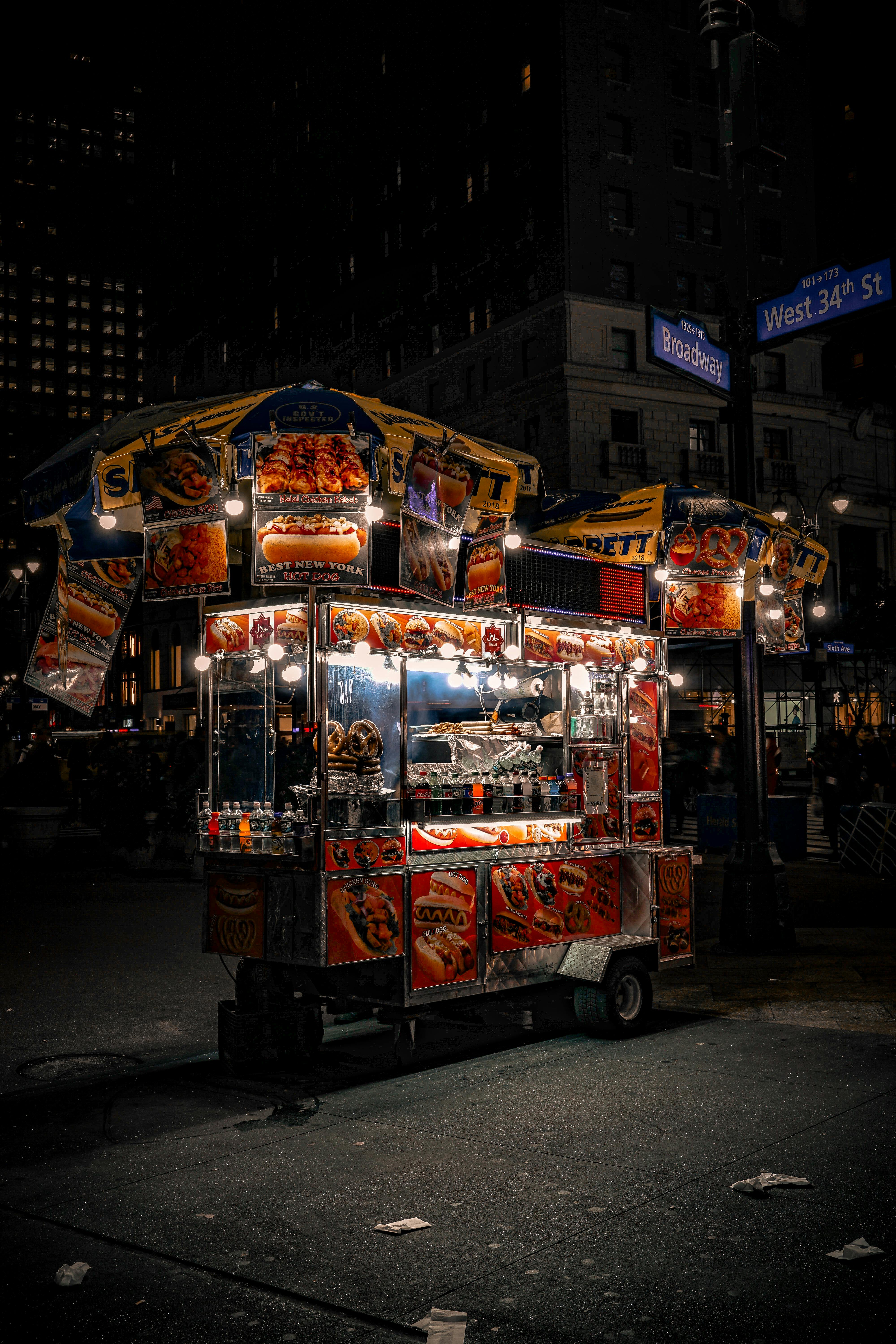 A vibrant New York food cart illuminated at night on Broadway and West 34th St.