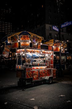 A vibrant New York food cart illuminated at night on Broadway and West 34th St.