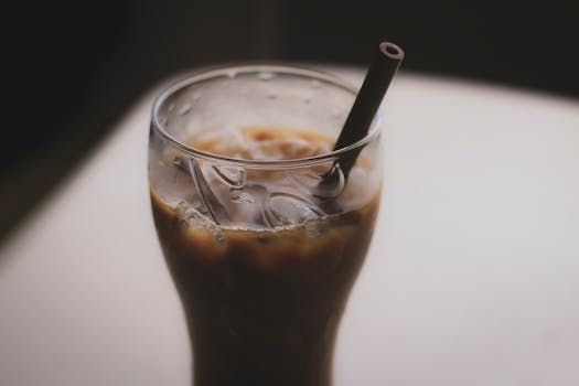 Close-up of an iced coffee with a straw on a table, emphasizing refreshment and taste.