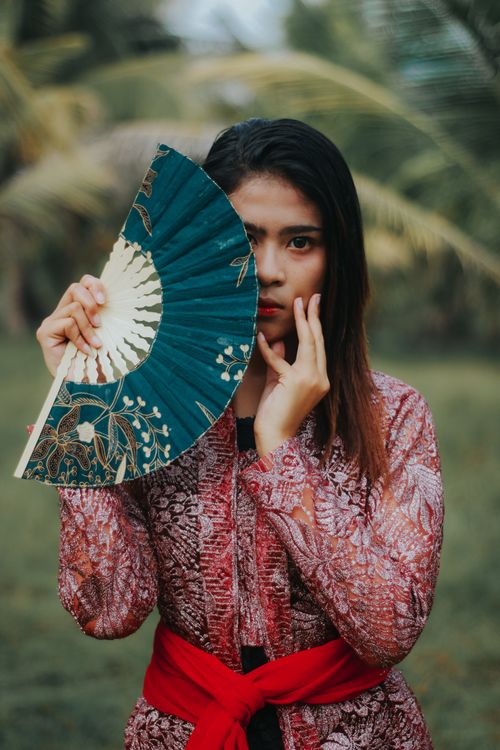 Free Portrait of an Asian woman holding a hand fan outdoors, showcasing traditional fashion. Stock Photo