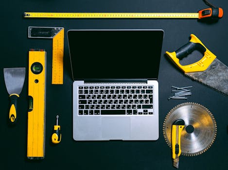 黑色背景下，一台笔记本电脑的俯视图周围环绕着各种手动工具，象征着技术与建筑