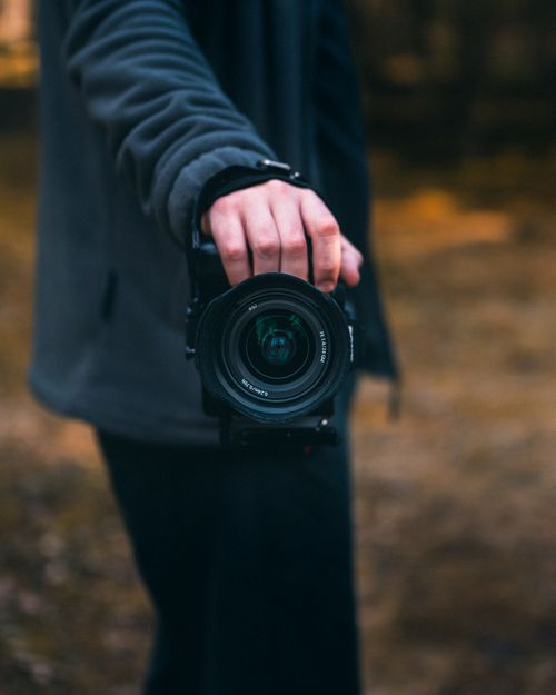 Free Person holding a DSLR camera against an outdoor background, showcasing photography gear. Stock Photo