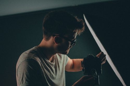 Free Photographer adjusting camera and equipment in a studio setting. Low light atmosphere. Stock Photo