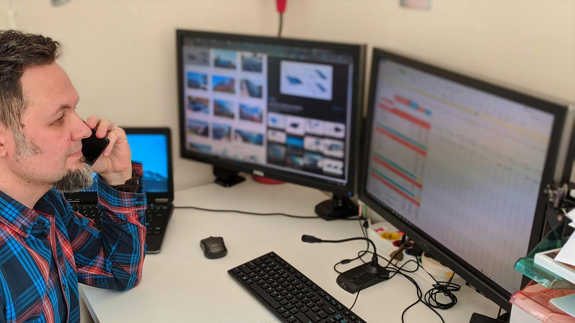 Businessman multitasking with computer screens and phone in a modern office environment.