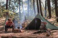 Hiker resting near fire and tent during travelling