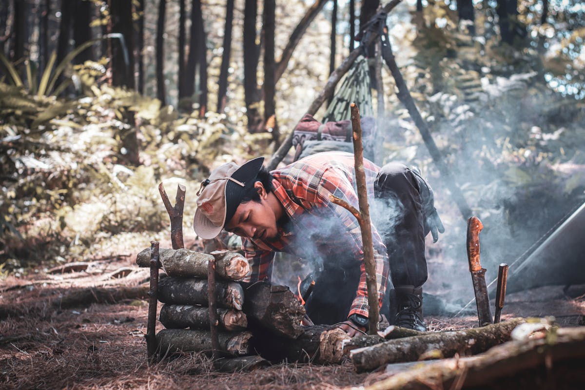 Ethnic man preparing bonfire in forest during expedition