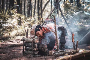Ethnic man preparing bonfire in forest during expedition