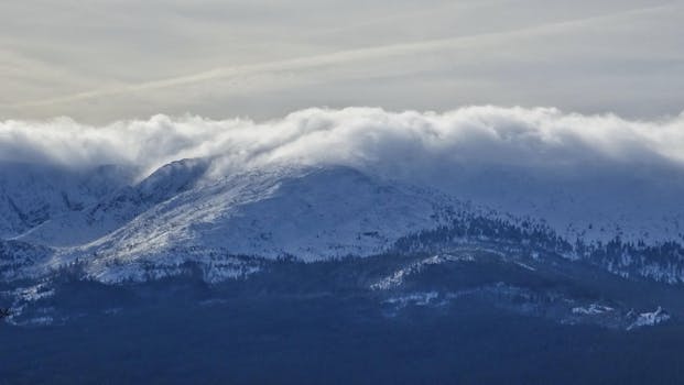 Stunning view of snow-covered mountains with clouds and winter landscape.