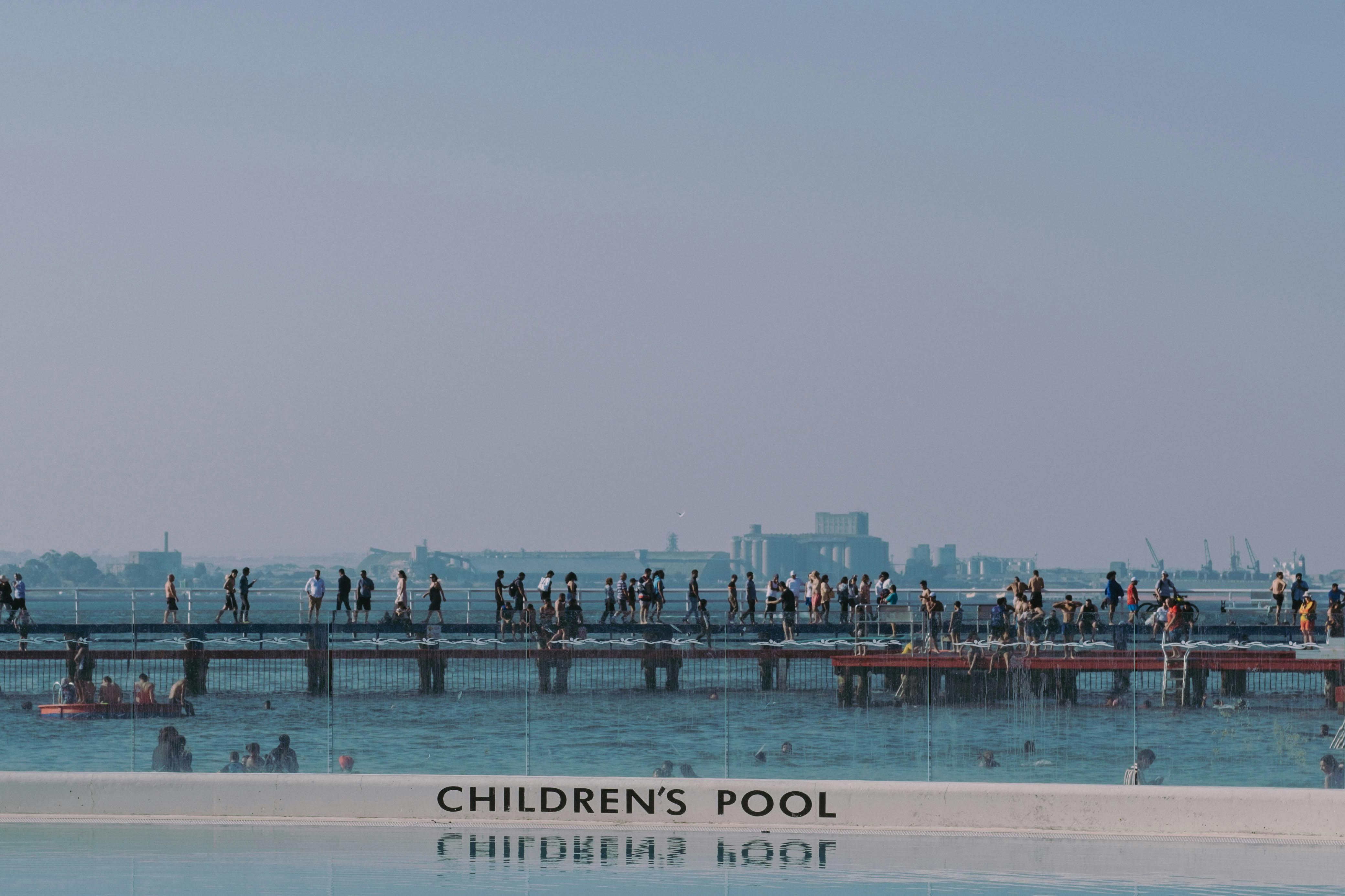 People enjoy a sunny day walking across the bridge at Geelong's waterfront children's pool area.