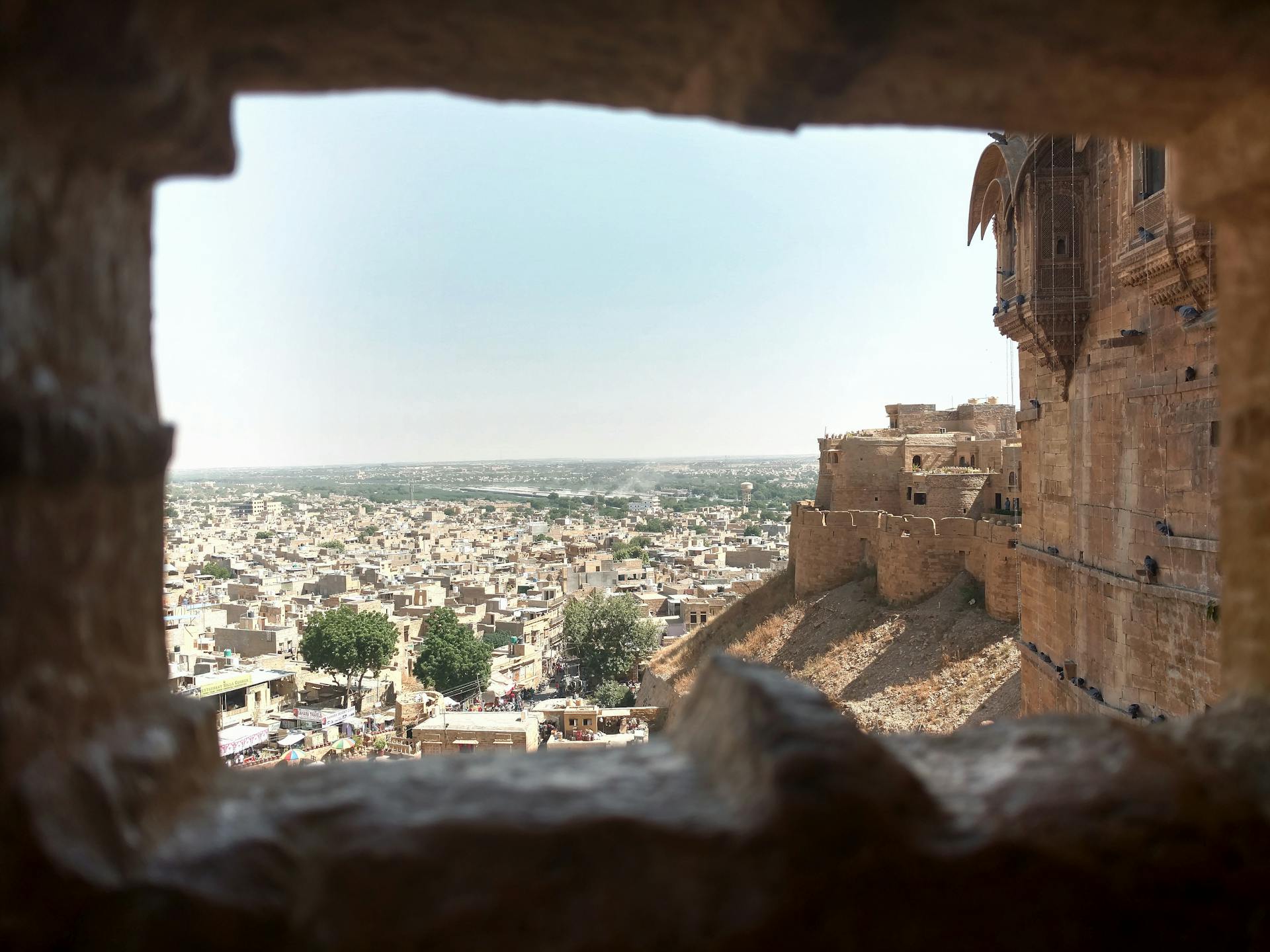 Distant ancient stone buildings of aged town with wall of medieval fort in India