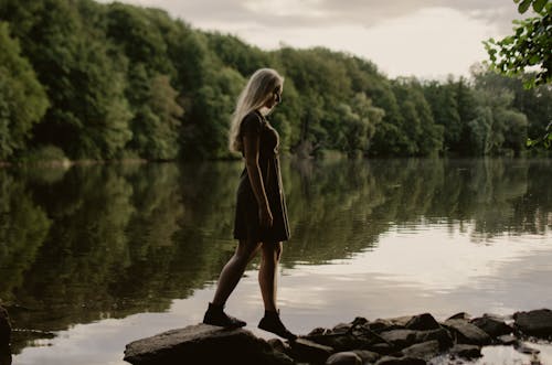 Young woman standing near lake in green forest