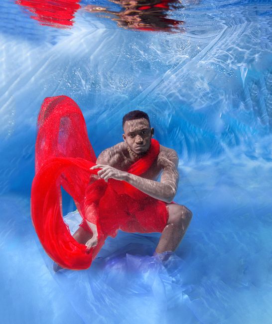 An artistic and vibrant underwater photo of a man wrapped in red fabric, creating dynamic movement.