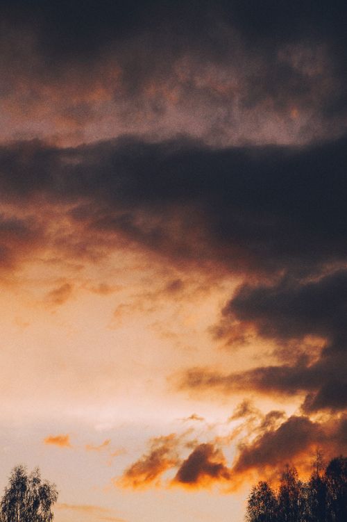 Free Vivid sunset sky with dramatic clouds turning shades of orange and dark grays. Stock Photo