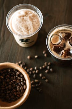 Close-up of iced coffee in plastic cups with coffee beans on a wooden table.