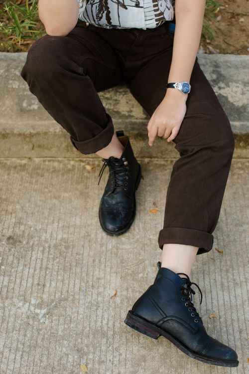 Free From above of crop unrecognizable male in casual pants and black boots sitting on concrete border on street Stock Photo