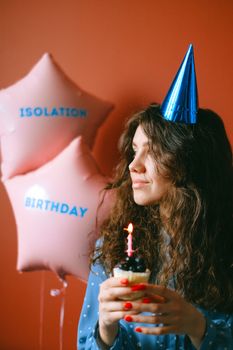 Adult woman celebrating her birthday alone indoors with cupcake and themed balloons.
