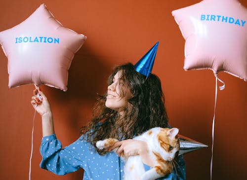 A Woman Carrying a Cute Tabby Cat while Looking at the Balloon on Her Side