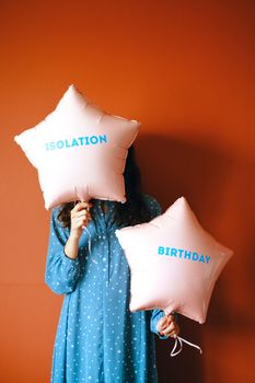 Woman holding star-shaped balloons labeled 'Isolation' and 'Birthday' against a vibrant orange background.
