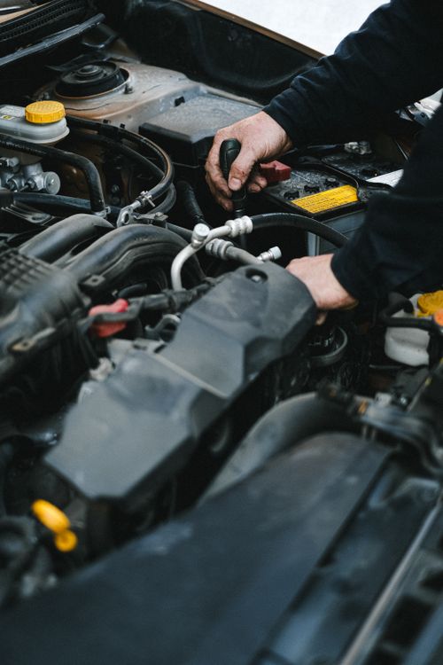 Free Close-up of a mechanic's hands working on a car engine in an indoor workshop setting. Stock Photo