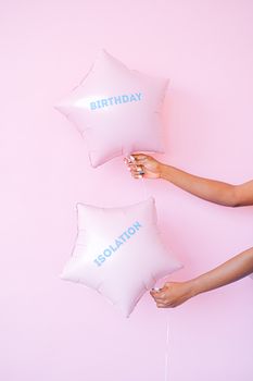 Star shaped balloons with 'birthday' and 'isolation' text held against a pink background.