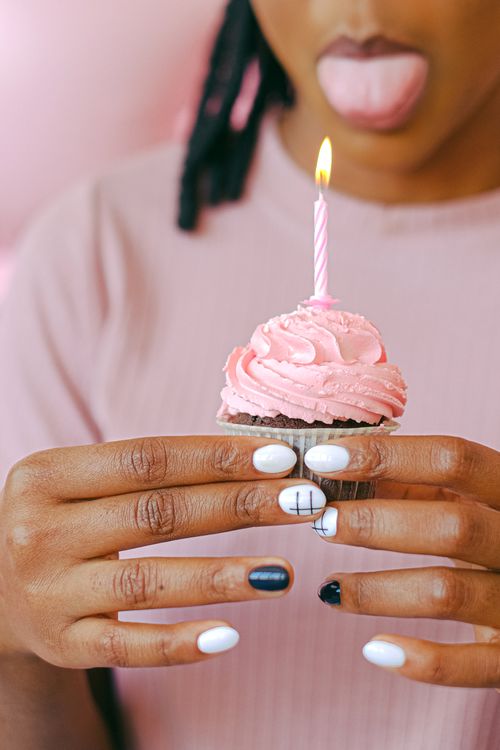 Free Close-up of a pink frosted cupcake with candle held by a person sticking out their tongue. Stock Photo