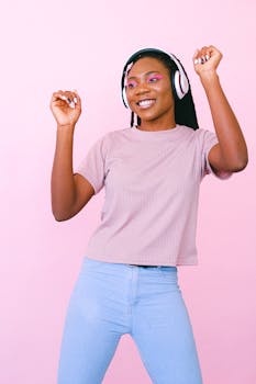 一名年轻女子戴着耳机，在柔和的粉色背景下随着音乐快乐地跳舞