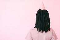 粉红色背景下，一个留着辫子、戴着派对帽的女人背影