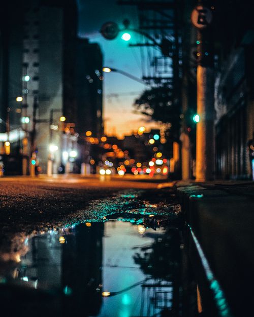 Free Ground level view of blurred modern illuminated road with water puddle reflecting buildings and sky in evening time in city Stock Photo