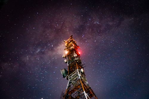 Free From below skyline of illuminated telecommunication tower under cloudless night sky with bright stars and Milky Way Stock Photo