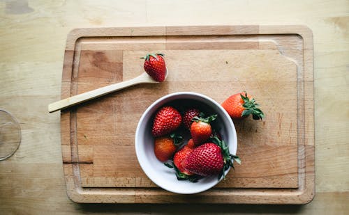 A Bowl of Strawberries Placed on Top of a Wooden Chopping Board