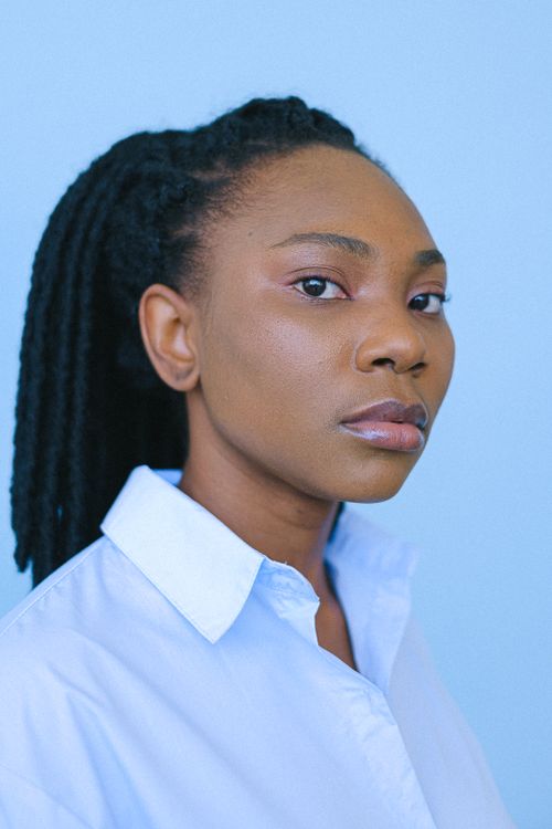 Free Close-up portrait of a woman with dreadlocks against a blue background wearing a white shirt. Stock Photo