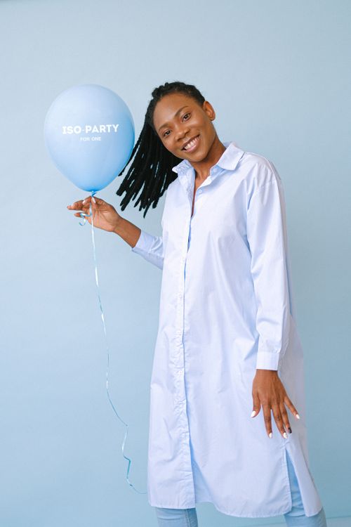 Free A smiling woman in a white dress holds a blue balloon against a blue background. Stock Photo