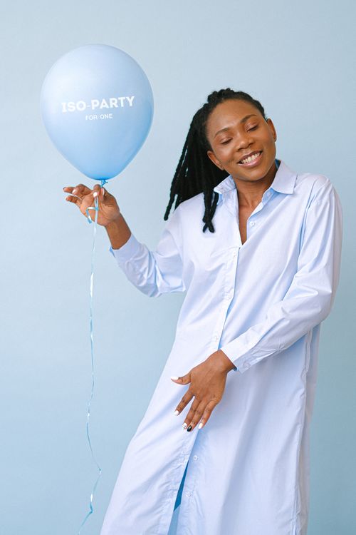 Free A happy African American woman in a white shirt holding a blue balloon labeled 'ISO-PARTY FOR ONE'. Stock Photo