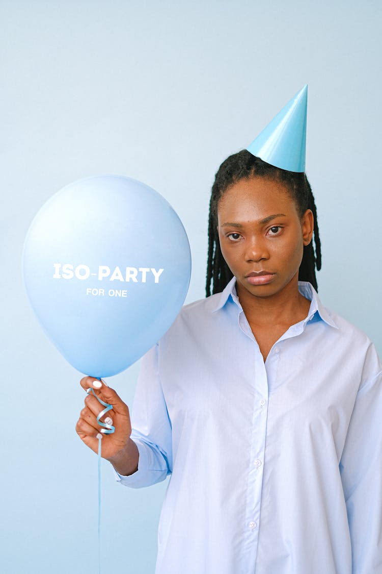 A Sad Woman Wearing Party Hat While Holding A Blue Balloon