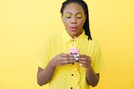 A Woman in Yellow Polka Dot Blouse Blowing the Lighted Candle on Top of a Cupcake