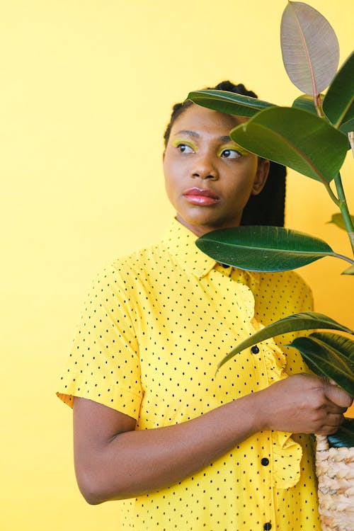 Free Woman in Yellow and Black Polka Dot Button Up Shirt Standing Near A Rubber Plant Stock Photo