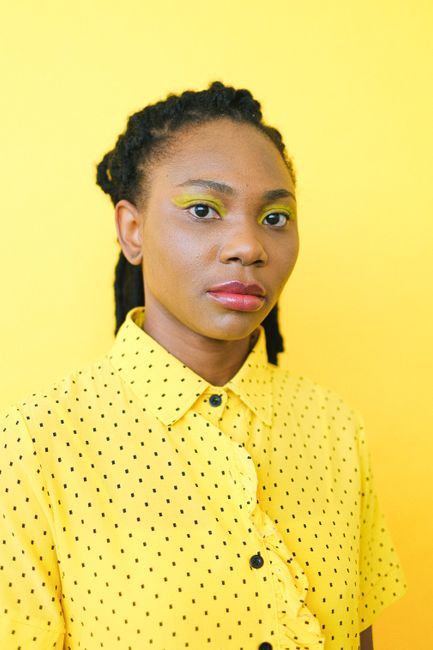 Bright portrait featuring a woman in a yellow polka-dot shirt with eye-catching makeup against a yellow background.