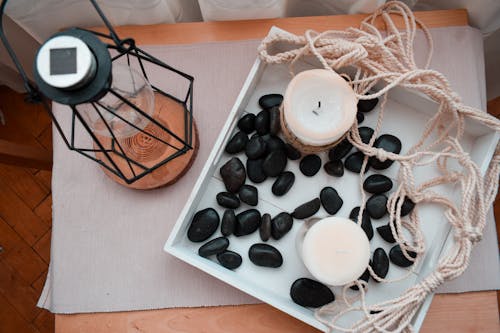 Scented Candles Surrounded by Black Rocks on a Wooden Tray