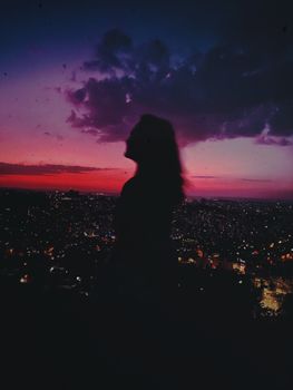 黄昏时分，一名女子的剪影凝视着充满活力的城市景观，宁静与神秘感油然而生