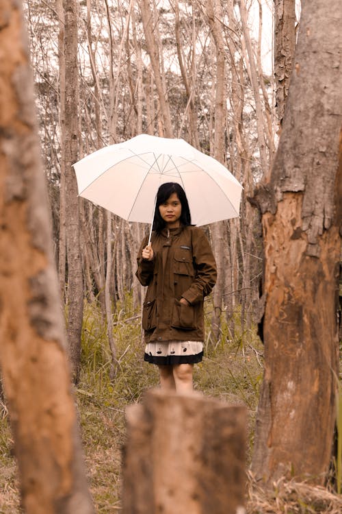 Young ethnic woman with umbrella standing in forest