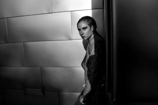 Black and white side view of trendy fashionable female looking at camera near glowing wall in house