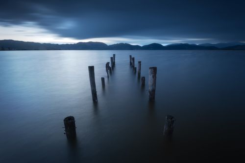 Free Calm twilight scene at Lake Massaciuccoli with wooden posts and distant mountains in Tuscany. Stock Photo