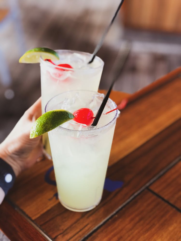 Crop Person With Bright Garnished Cocktails In Cafe