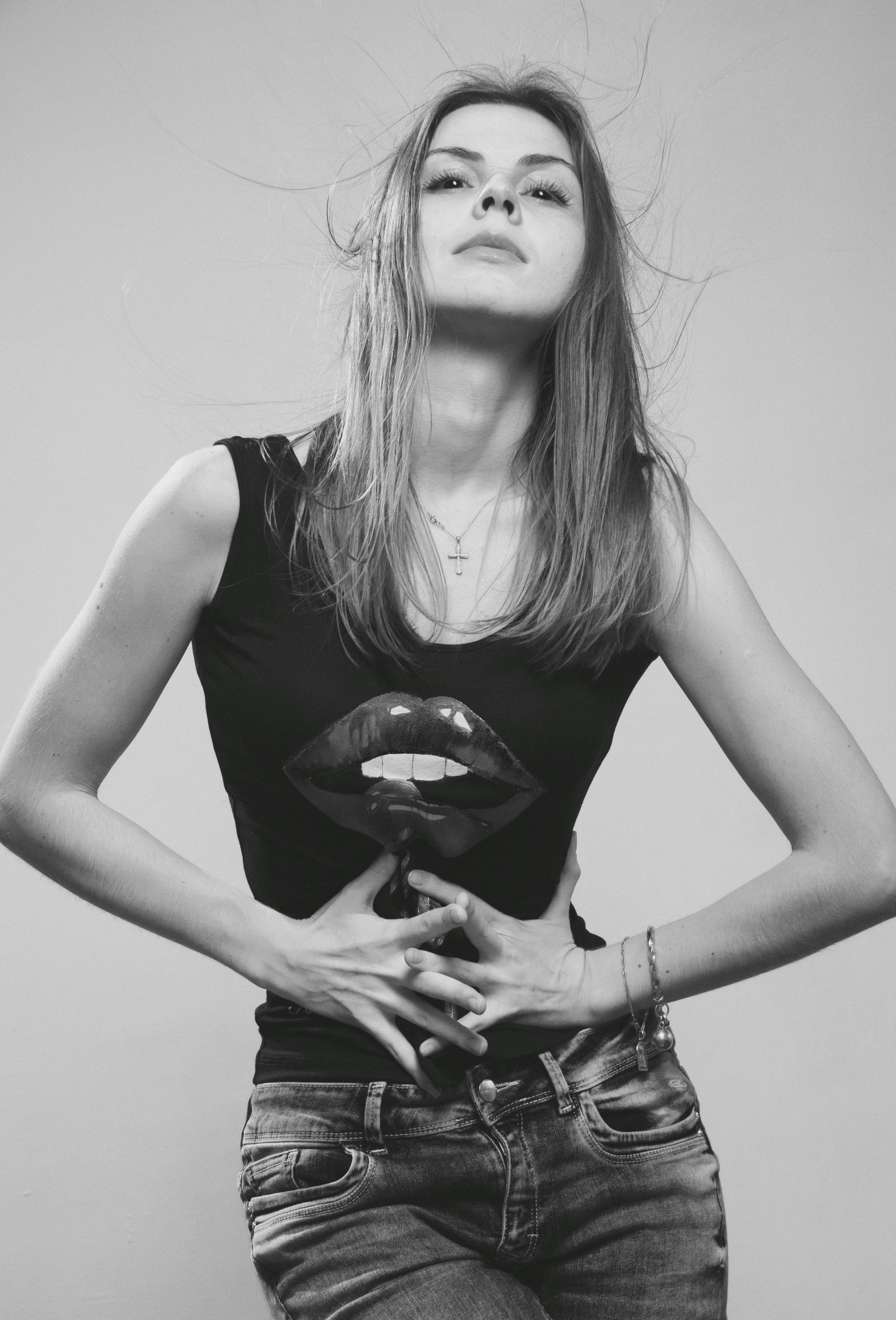 Black and white photo of a confident young woman posing with hands on waist, exuding elegance and style.