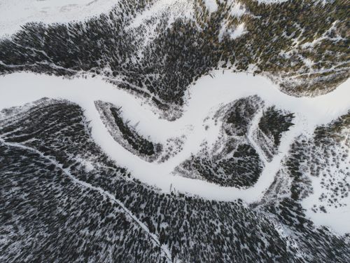 Free Top view of frozen river flowing through coniferous forest covered snow in winter day Stock Photo