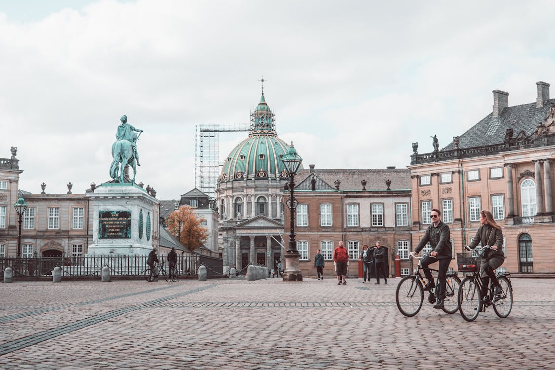 Free Aged masonry cathedral and sculpture near buildings on tiled pavement with walking people in Copenhagen Stock Photo