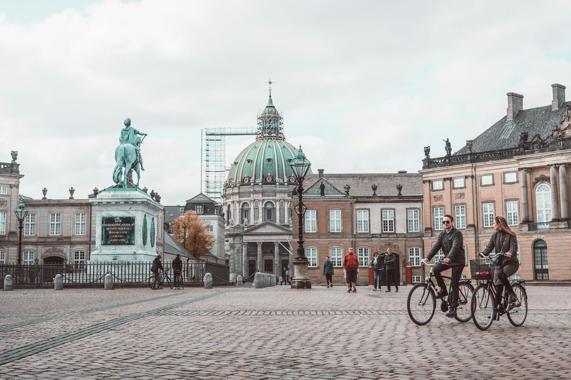 Aged masonry cathedral and sculpture near buildings on tiled pavement with walking people in Copenhagen