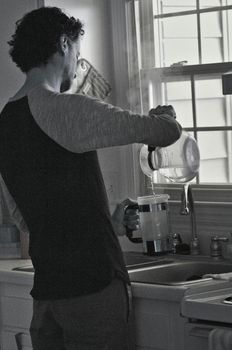 Black and white image of a man using a coffee press by a window.
