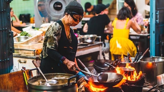 Experienced chef skillfully cooking over open flames in Bangkok's bustling street market.