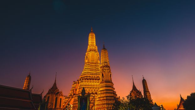 Stunning view of Wat Arun temple in Bangkok at sunset, capturing its golden glow against the twilight sky.
